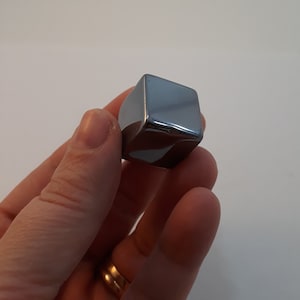 Op de afbeelding: Een enkele, vierkante, metalen ijsblokje. De blokje is gemaakt van roestvrij staal en heeft een glanzend, reflecterend oppervlak.