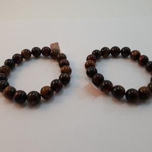 Puede incluir: Dos pulseras de cuentas marrones, negras y doradas. Las cuentas son redondas y tienen un patrón de ojo de tigre.