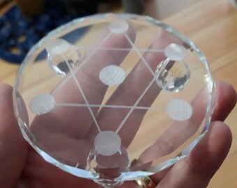 Puede incluir: Una base de cristal de vidrio transparente con un diseño geométrico grabado en la superficie. La base tiene cuatro patas de cristal.