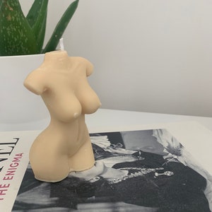 May include: A nude-colored candle shaped like a human torso. The candle has a white wick.