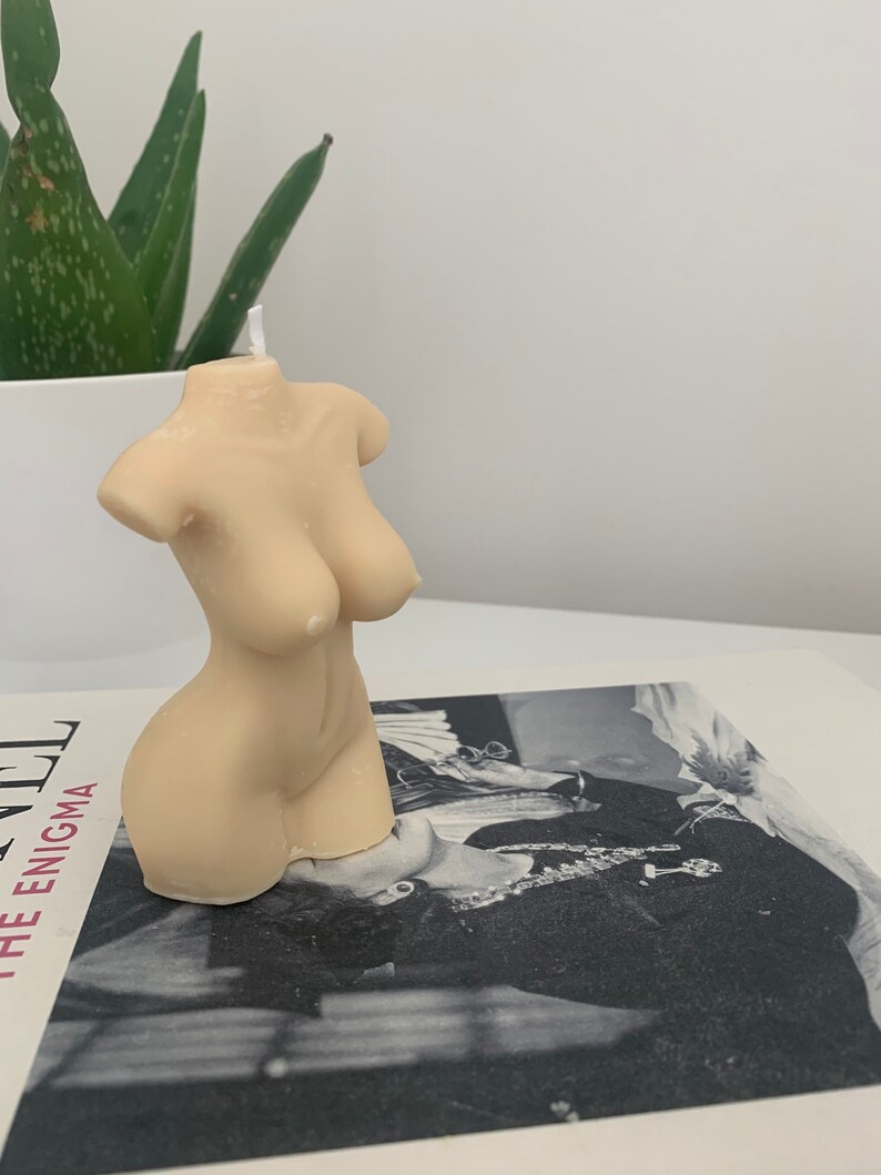 May include: A nude-colored candle shaped like a human torso. The candle has a white wick.