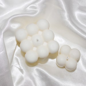 May include: Two white bubble candles, one large and one small, on a white satin background.