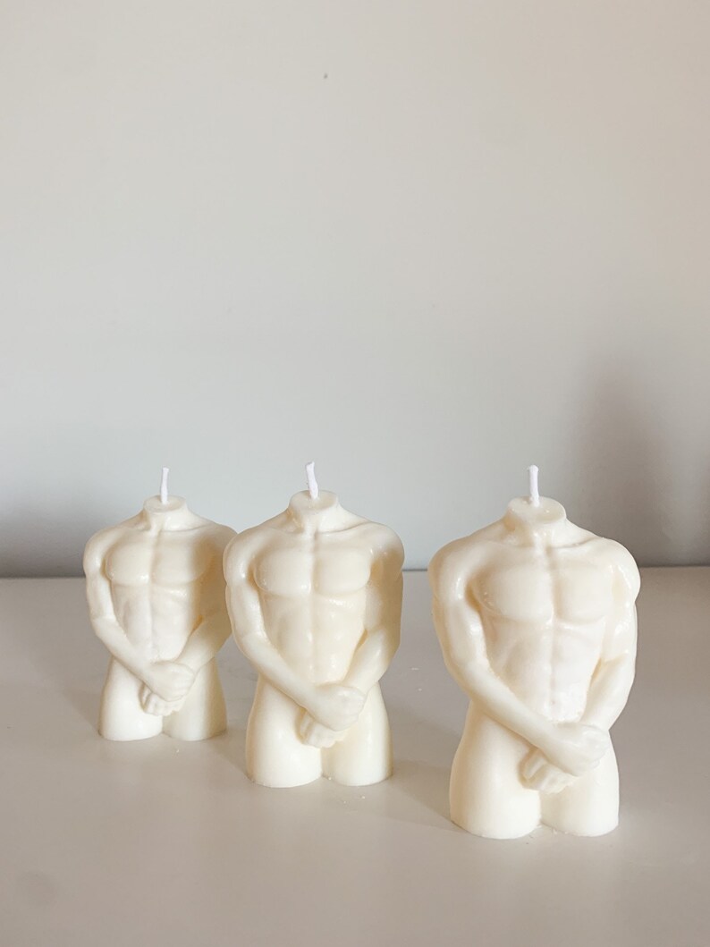 May include: Three white sculpted candles shaped like a human torso. The candles are standing on a white surface.