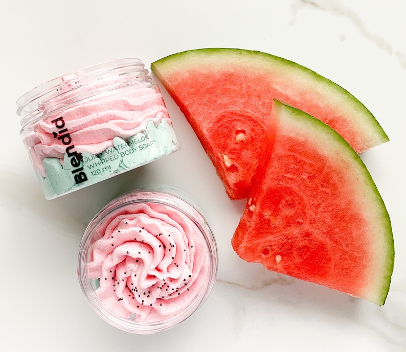 May include: Two clear jars of pink and green whipped body soap with the text "blendid juicy watermelon whipped body soap 120 ml" on the jar. Two slices of watermelon are on a white marble surface.
