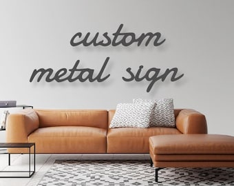 May include: A brown leather couch with a matching ottoman in front of a white wall. The wall has a custom metal sign that reads "custom metal sign" in a cursive font.