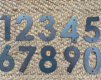 May include: Ten black metal house numbers, 1 through 10, on a woven brown background. The numbers are all the same size and style, with a slightly rounded font.