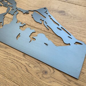 May include: A metal cutout of a mountain range, with a gray finish. The cutout is on a wooden surface.
