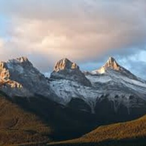 May include: Three snow-capped mountain peaks rise against a cloudy sky, with a forest in the foreground.