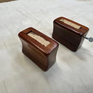 Könnte beinhalten: Zwei dunkelbraune Holzmöbelfüße. Jeder Fuß hat eine rechteckige Form mit einer helleren Holzeinlage und einer Metallschraube. Diese Füße sind für die Befestigung an Möbeln konzipiert.