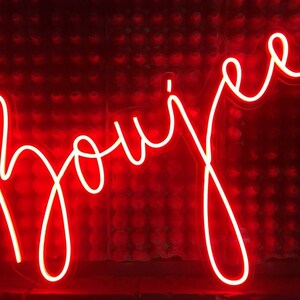 K&ouml;nnte beinhalten: Ein Neon-Schild mit dem Wort "Boujee" in wei&szlig;en Buchstaben vor einem roten Hintergrund.