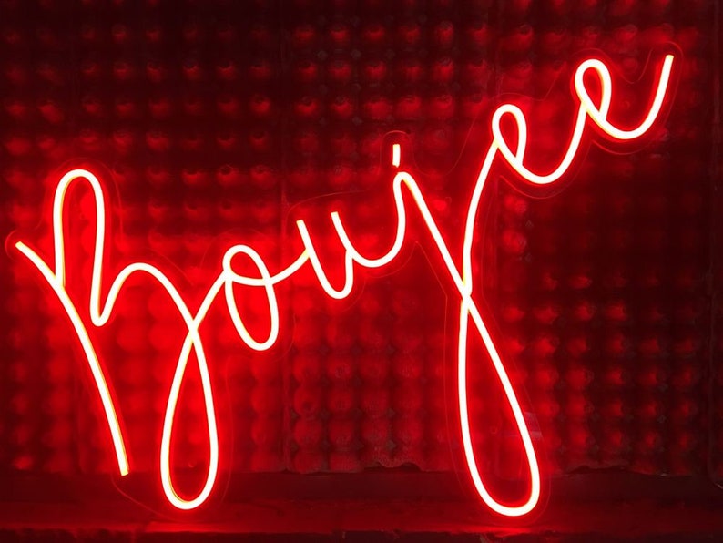 K&ouml;nnte beinhalten: Ein Neon-Schild mit dem Wort "Boujee" in wei&szlig;en Buchstaben vor einem roten Hintergrund.