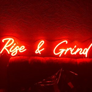 K&ouml;nnte beinhalten: Rotes Neon-Schild mit den Worten "Rise & Grind" in kursiv.
