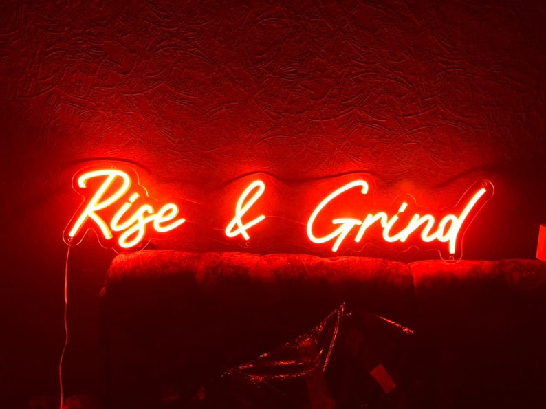 K&ouml;nnte beinhalten: Rotes Neon-Schild mit den Worten "Rise & Grind" in kursiv.