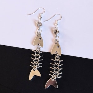 May include: Silver fishbone earrings with a dangling fishtail charm. The earrings are made of metal and have a silver finish.