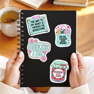 May include: A black spiral-bound notebook with four colourful stickers. The stickers feature phrases like "The way to my heart is through the bookstore," "Endless TBR," "Uh oh... I bought more books," and "Reading is my jam."