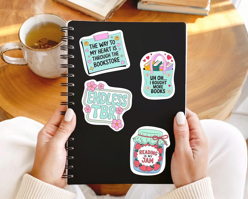 May include: A black spiral-bound notebook with four colourful stickers. The stickers feature phrases like "The way to my heart is through the bookstore," "Endless TBR," "Uh oh... I bought more books," and "Reading is my jam."