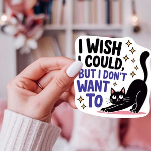 K&ouml;nnte beinhalten: Wei&szlig;er Aufkleber mit dem Text &bdquo;I wish I could, but I don't want to&ldquo; und einer Illustration einer schwarzen Katze. Die Katze streckt sich mit erhobenem Schwanz. Goldene Sterne umgeben Text und Katze.