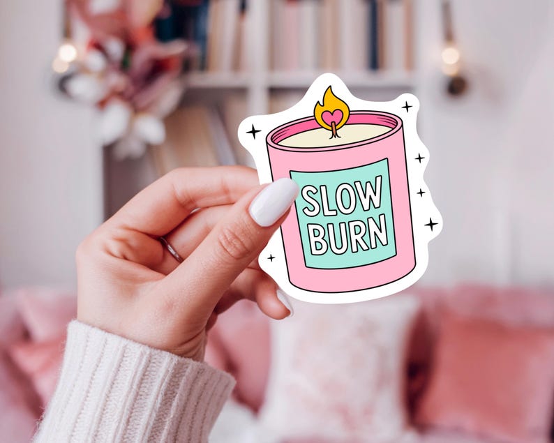 May include: A pink candle sticker with a light blue label that reads "SLOW BURN" in white text. The candle has a yellow flame with a heart shape in the middle. Black star accents surround the sticker.