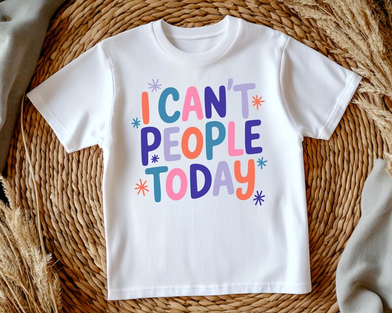K&ouml;nnte beinhalten: Wei&szlig;es T-Shirt mit dem Schriftzug "I CAN'T PEOPLE TODAY" in farbenfrohen, verspielten Buchstaben. Der Text ist in verschiedenen Farben gehalten, darunter T&uuml;rkis, Orange, Lila, Pink und Blau, mit Sternakzenten. Das Shirt wird auf einem gewebten Hintergrund pr&auml;sentiert.