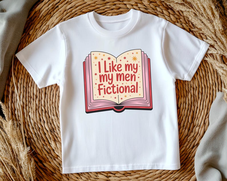 May include: White t-shirt with a graphic of an open book. The book design has a pink border and gold star accents, and the text reads "I Like my men Fictional" in red and pink.