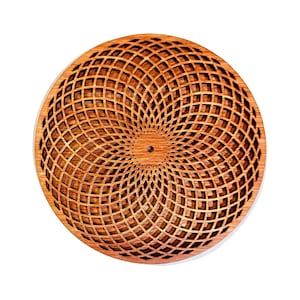 May include: A circular wooden coaster with a geometric pattern of concentric circles and squares, creating a swirling effect. The coaster is made of light brown wood and has a smooth, polished finish.