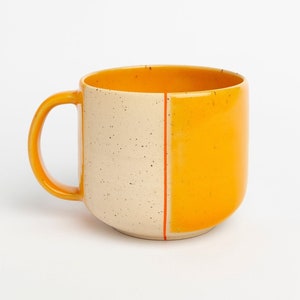 Könnte beinhalten: Eine Keramiktasse mit einem gesprenkelten weißen und gelben Überzug. Die Tasse hat einen Henkel und eine rote Linie an der Seite.