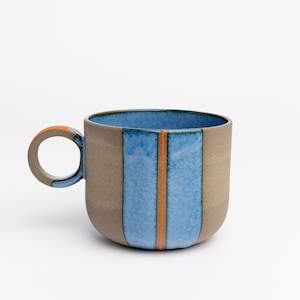 以下が含まれることがあります： 茶色の外側と青い内側を持つセラミック製のマグカップ。マグカップの中央にはオレンジ色のストライプが1本入っています。