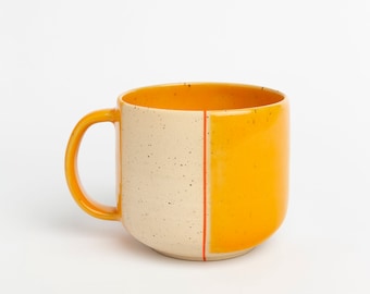 May include: A ceramic mug with a speckled white glaze and a solid yellow glaze. The mug has a red line down the center and a rounded handle.