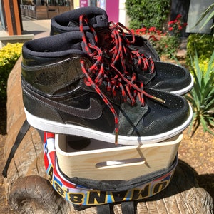 Könnte beinhalten: Schwarze Lackleder-High-Top-Sneaker mit roten und schwarzen Schnürsenkeln. Die Sneaker sitzen auf einer Holzkiste mit einem bunten Rucksack darunter.