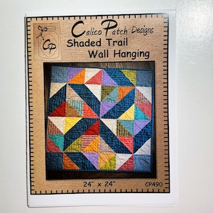 May include: A printed pattern for a "Shaded Trail Wall Hanging" quilt, 24 x 24 inches. The quilt design features a geometric pattern of colorful triangles in shades of blue, orange, yellow, purple, and green. The pattern is by Calico Patch Designs.
