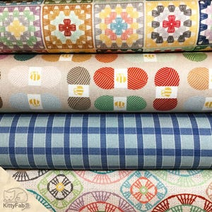 May include: A stack of fabric rolls with various patterns. The top roll features a patchwork design in shades of yellow, brown, and pink. Below are rolls with yarn ball prints, blue gingham, and a floral design. The KittyFab logo is visible.