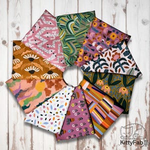 May include: A circular arrangement of fabric pieces with various floral and geometric patterns. The fabrics feature colors like pink, green, orange, and brown. The fabrics are arranged on a light wood surface.