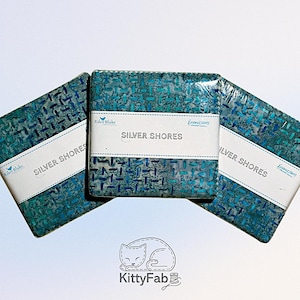 May include: Three square fabric bundles with a teal and blue patterned design. Each bundle is wrapped in clear plastic and has a white label that reads "Silver Shores". The Riley Blake and Expressions logos are also visible.