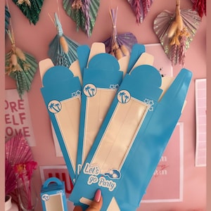 May include: A set of four blue cardboard boxes with a window and a handle. The boxes have a palm tree design and the text "Let's go Party".