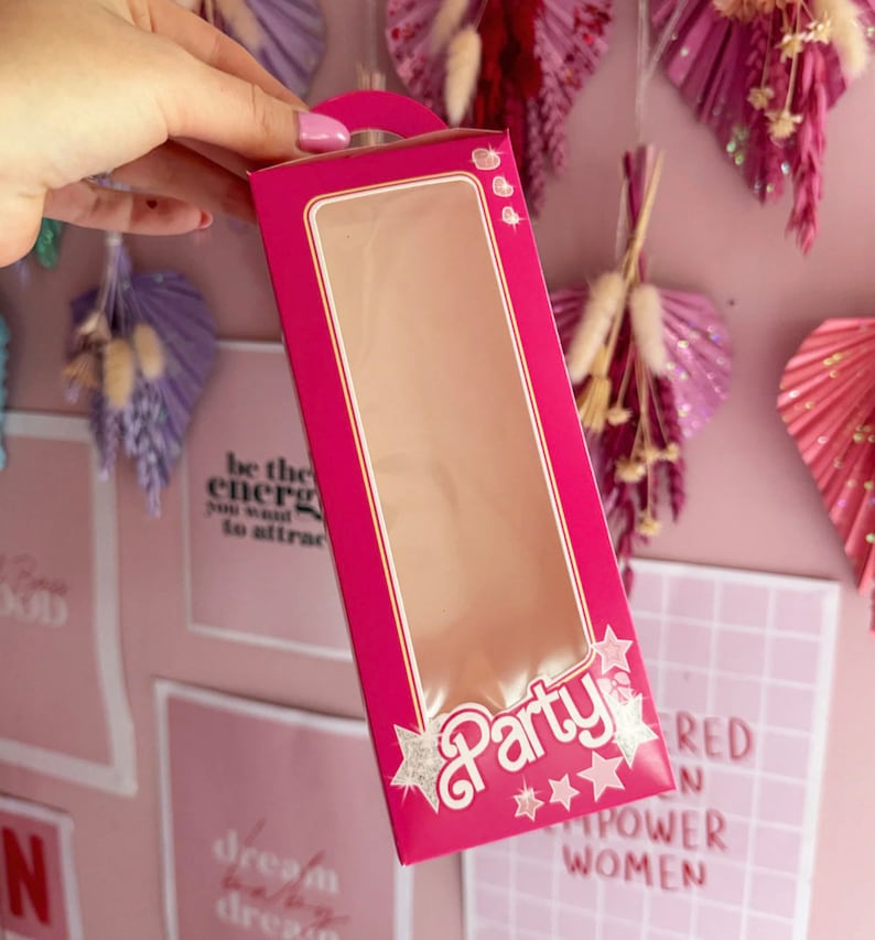 May include: Pink cardboard box with a clear window, featuring the word "Party" in white with silver glitter stars. The box has a handle on the top.