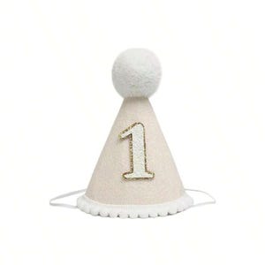 May include: A white and gold party hat with a fluffy white pom-pom on top and the number "1" in gold glitter.