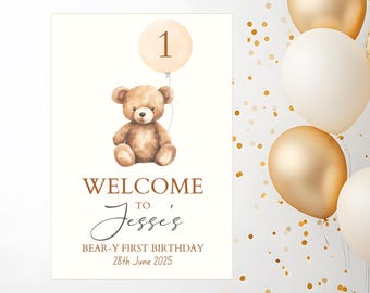 May include: A welcome sign for a first birthday celebration. The sign features a watercolor illustration of a teddy bear holding a balloon with the number 1. The text reads "WELCOME TO Jesse's BEAR-Y FIRST BIRTHDAY 28th June 2025."