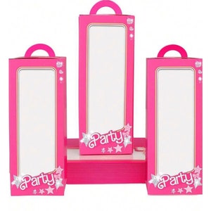 May include: Three pink party favor boxes with a clear window and a handle. The boxes have a pink and gold border and the words "Party" with stars and glitter.