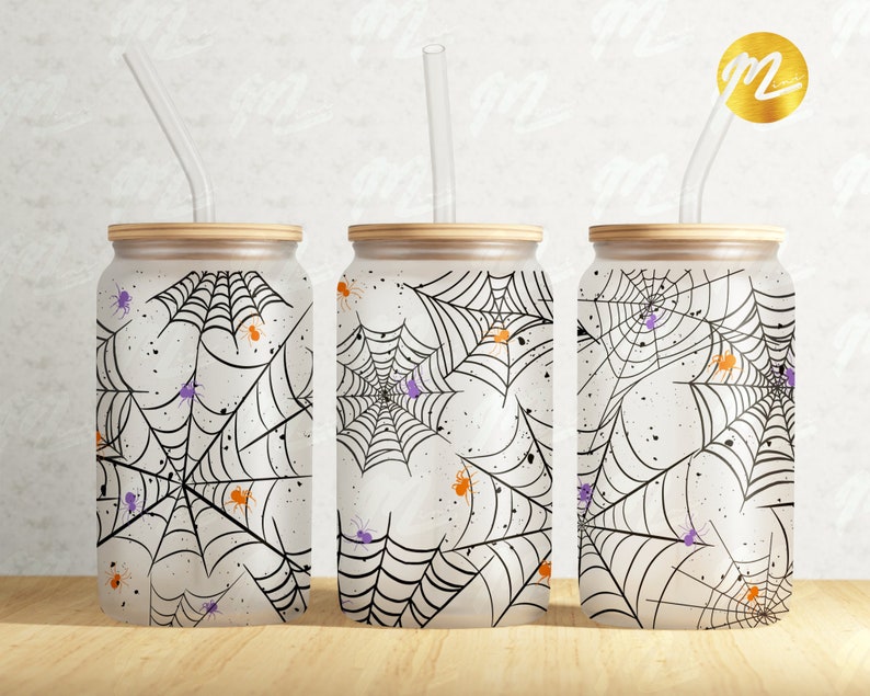 Puede incluir: Tres vasos blancos con telara&ntilde;as negras y ara&ntilde;as naranjas y moradas impresas en ellos. Cada vaso tiene una pajita de pl&aacute;stico transparente.