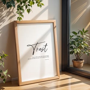 Könnte beinhalten: Ein gerahmter Druck mit dem Wort "Trust" in eleganter schwarzer Schrift. Der Druck enthält auch den Text "Vertraue dem Herrn von ganzem Herzen und verlasse dich nicht auf deinen eigenen Verstand." Der Rahmen ist hellbraun.