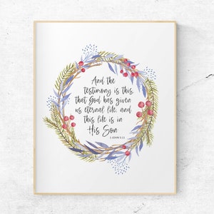 May include: A watercolor illustration of a wreath with blue and green leaves and red berries. The wreath surrounds a quote from the Bible: "And the testimony is this, that God has given us eternal life, and this life is in His Son. 1 John 5:11"