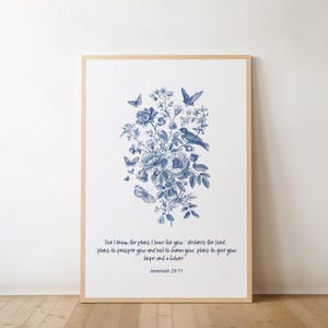 Puede incluir: Impresión artística enmarcada con un diseño floral azul, mariposas y un pájaro. La impresión incluye el texto "For I know the plans I have for you...Jeremiah 29:11". El marco es de color madera clara.
