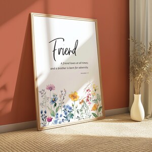 Könnte beinhalten: Ein gerahmter Druck mit dem Wort „Freund“ in eleganter Schrift. Der Druck zeigt einen floralen Rand mit bunten Aquarellblumen. Der Text lautet: „Ein Freund liebt allezeit; und ein Bruder wird für die Not geboren.“