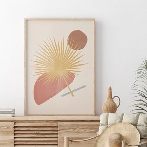 May include: A minimalist art print featuring a stylised palm leaf in shades of gold and brown, with abstract shapes in shades of pink and grey on a cream background.