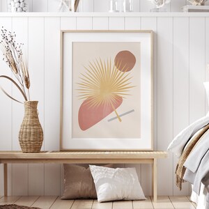 May include: A framed print with a minimalist design featuring a stylised palm leaf in gold, a pink and a brown circle on a beige background.