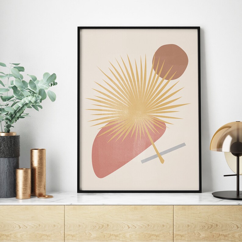 May include: Abstract art print featuring a stylised palm leaf in shades of yellow and brown, with geometric shapes in pink and brown on a cream background.