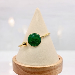 May include: A gold bangle bracelet with a green round stone. The bracelet is on a white display stand.