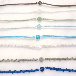 May include: A collection of ten bracelets with different coloured cords and gemstone beads. The beads include brown, red, grey, white, green, blue, turquoise, pearl, grey, and blue.