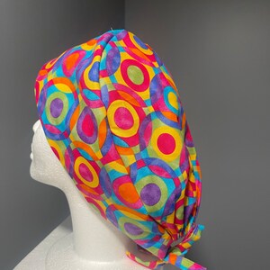 Op de afbeelding: Een kleurrijke chirurgische scrub-muts met een geometrisch patroon van overlappende cirkels in tinten roze, geel, oranje, blauw en paars.