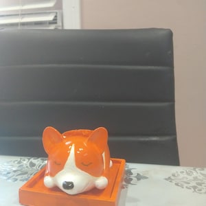May include: Orange and white ceramic figurine of a sleeping dog with closed eyes. The figurine is on a square orange base.